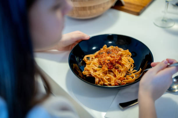 Unrecognizable female person holding a black plate with pasta and tomato sauce on the table.