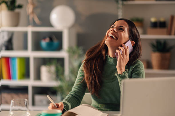 istock Laughing woman talking on a smartphone while taking notes during a phone call 1953033282