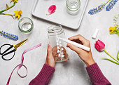 Step 2. Paint a plant motif on a glass jar with white acrylic painter. Making spring decor for Easter or Mother's Day with kids.
