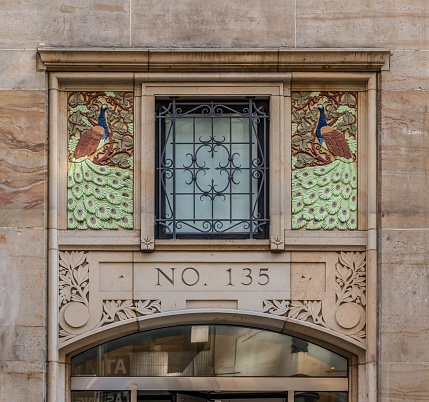 The transom above the main entrance to the Fashion Tower at 135 W 36th Street in the Garment Center is elaborately decorated, included two colorful terra cotta peacocks. 

The 17-story building, completed in in 1922, was designed by architect Emory Roth. 

Most people, New Yorkers and visitors alike, view the Garment District as dull and gray, grim even. 

But architecturally, at least, the Garment District can be interesting and even whimsical. Keep a sharp lookout upward as you walk through the District and you'll find trolls, grotesques, and mascarons. You'll also find a variety of old-fashioned craftsmanship, from intricate bricklaying to marble, granite, and terra-cotta sculpture.