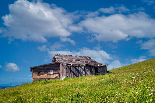 Small old wooden hut cabin in mountains on green pasture against blue sky