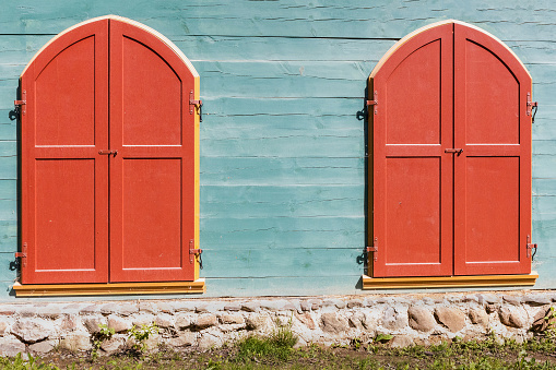Two old red painted wooden doors on a blue wooden wall with foundations during the day