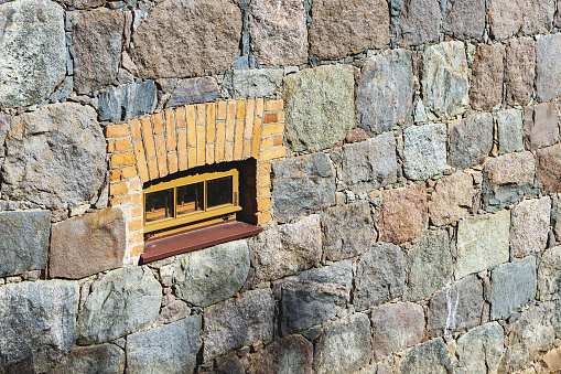 An ancient small window on a stone wall with bricks on a sunny day