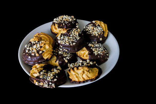 A bunch of biscuits on a plate covered with chocolate and peanut crumbs on a black background