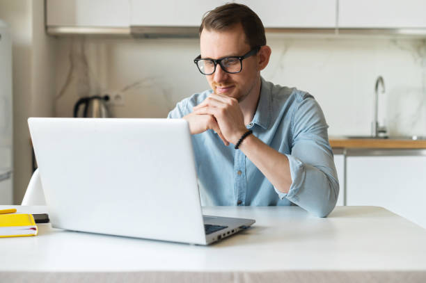 istock Concentrated young man wearing stylish eyewear working with a laptop remotely 1953116487
