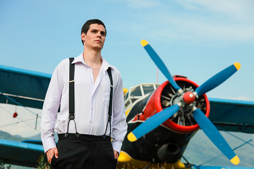 Young man standing in front of a propeller airplane on an airport. Antique fashion.