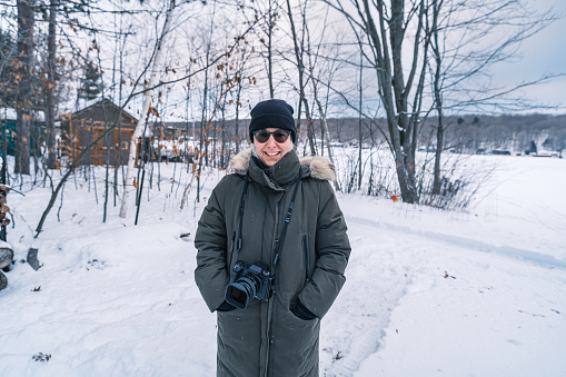 Mature woman enjoying winter outdoors. She is  dressed in warm winter outdoor clothing, wearing camera around her neck. Exterior of Lake House in Georgian Bay area of Ontario, Canada.