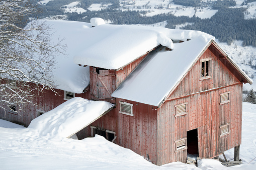 Old wooden barn with a snowy field in the foreground. Cloudy skies are above.