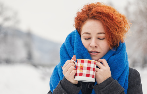 Beautiful young woman drinking hot cocoa outdoors during holidays