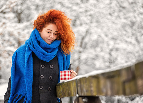Beautiful young woman drinking hot cocoa outdoors during holidays