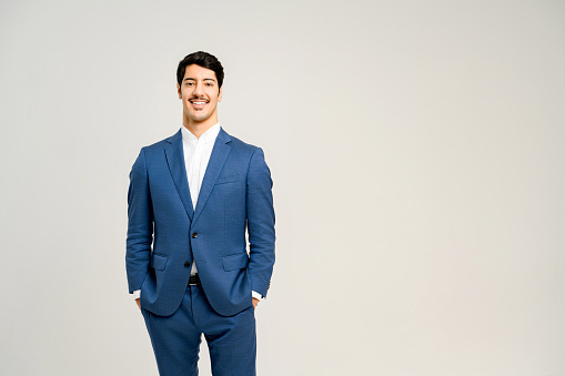 A confident young Hispanic man in a tailored blue suit stands with his hands in his pockets, exuding a sense of approachability and professionalism, perfect for business or formal representations.