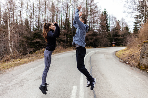 Happy Caucasian runners giving high five during running in nature on cold weather. Shot of a sporty young couple high fiving while exercising outdoors.