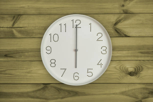 Plain white wall clock showing 6 pm on a wooden background. End of working day. Opening or closing hours. Schedule or working, study hours.