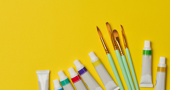 Tubes with oil paint and brushes on a yellow background, top view