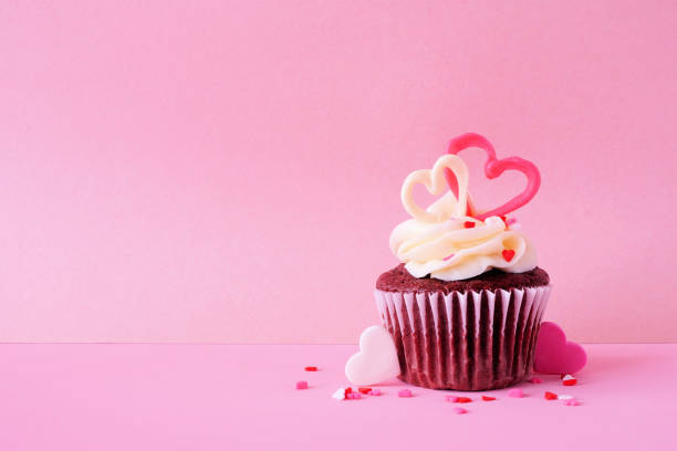 кекс из красного бархата на тему дня святого валентина с милыми сердечками и белой глазурью. вид сбоку на розовом фоне. - cupcake valentines day cake heart shape стоковые фото и изображения