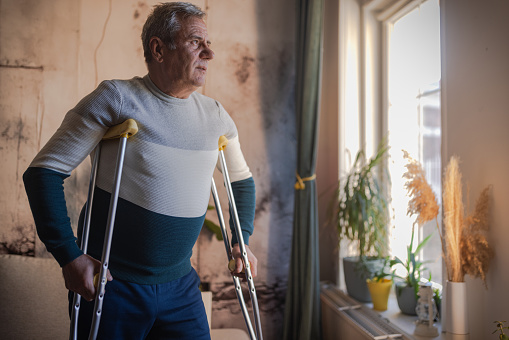 An elderly man walks with the help of crutches