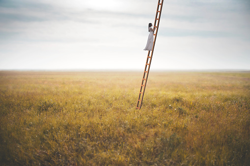 woman climbing a surreal ladder in the middle of a field reaching the sky, abstract concept