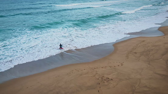 Unknown surfer entering sea aerial shot. Surfboarder shilouete putting board on water stepping foamy ocean super slow motion. Wonderful landscape with marine waves view. Active hobby leisure concept