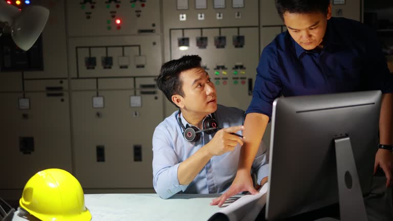 Technology Unleashed: Asian Engineers Engaged with Computer and Plan in Electric Control Room