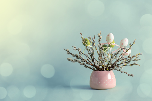 Easter eggs and pussy willow twigs with catkins in a vase. Beautiful defocused bokeh background. Space for copy.