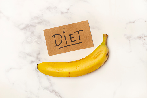 One banana with a diet sign on a white and gray marble kitchen counter in a top view