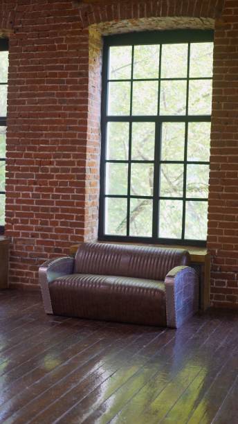 istock Brownish brick wall with leather sofa. Background photo with copy space for text. Claret leather sofa to the loft an interior with a bright searchlight and a window. brick wall. Leather sofa in a brick loft. 1953437760