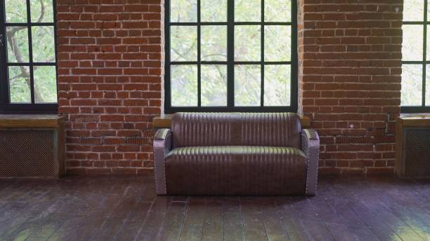 istock Brownish brick wall with leather sofa. Background photo with copy space for text. Claret leather sofa to the loft an interior with a bright searchlight and a window. brick wall. Leather sofa in a brick loft. 1953441862