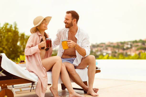 istock Beautiful young couple drinking juice by the pool 1953477427