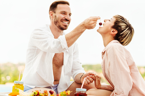 Beautiful young married couple eating fruits by the swimming pool on a hot summer day