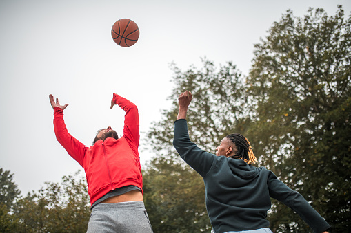 Action-packed scene as a Black male and a Hispanic male face off in the jump ball during their outdoor basketball match.