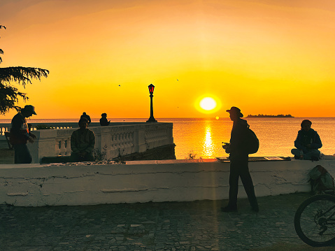 colonia del sacramento, uruguay - november 1 2022: people walking on boulevard and admiring the vibrant sunset over the Rio de la Plata