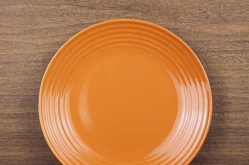 Empty orange plate on wooden background.