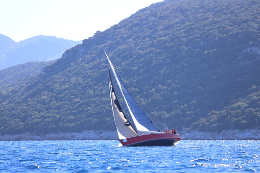 Bodrum,Turkey. January 14, 2024: sailor team driving sail boat in motion, sailboat wheeling with water splashes, mountains and seascape on background. Sailboats sail in windy weather in the blue waters of the Aegean Sea, on the shores of the famous holiday destination Bodrum