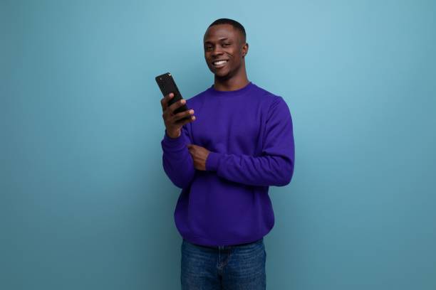 istock handsome young african guy in blue sweatshirt is using phone 1953608848