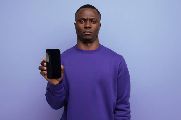istock authentic handsome young african man in blue sweater holding smartphone vertically with mockup for advertisement on blue background with copy space 1953608854
