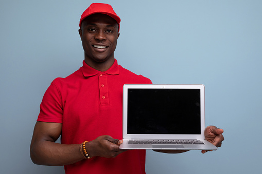 branded clothing concept. american man in red t-shirt and cap showing ads on laptop screen.