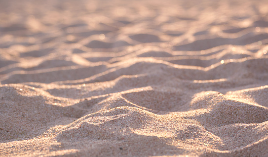 Close up of clean yellow sand surface covering seaside beach illuminated with evening light. Travel and vacations concept.