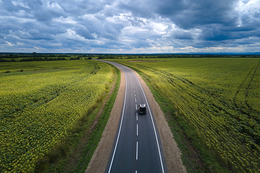 Aerial view of intercity road between green agricultural fields with fast driving car. Top view from drone of highway traffic.