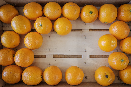 A top view of a semi-full wood crate of ripe oranges.