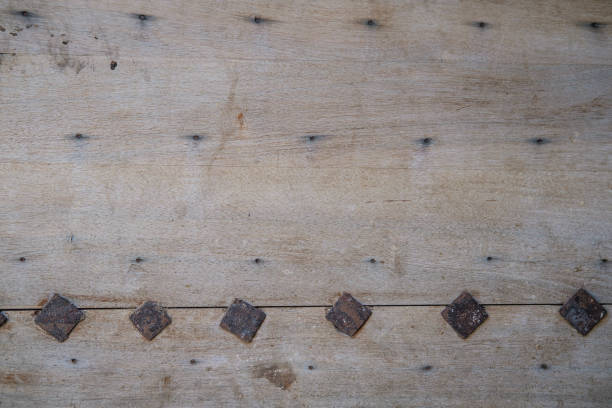 A distressed and weathered wood surface with a row of square iron nailheads at the bottom.