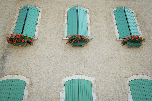 Three identical, slightly open teal wood shutters with hanging planters full of pink flowers.
