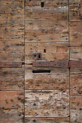 An old, weathered antique wood door with two rusty keyholes and a doorhinge.