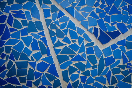 Close-up of a mosaic wall of vibrant blue tile with white cracks running through it.