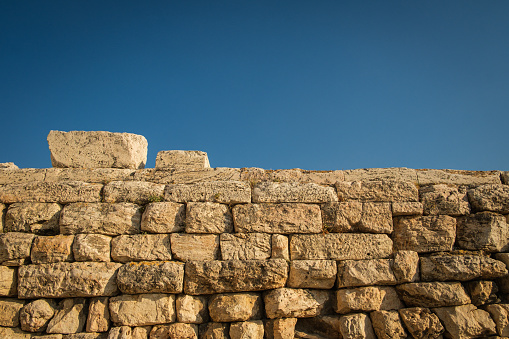A stone wall of the Parthenon in Greece, against blue sky.