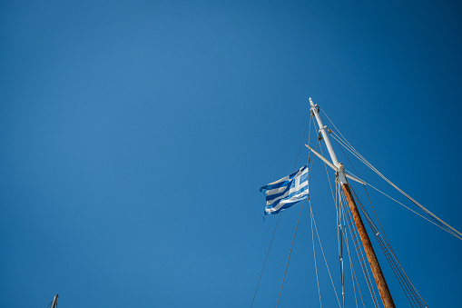 Sail boat mast with a waving Greek flag against a cloudless blue sky.