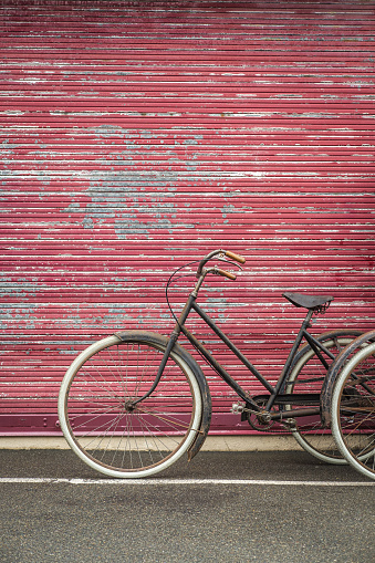 An old rusty gray bicycle with white tires parked in front of a chipped red metal garage door.
