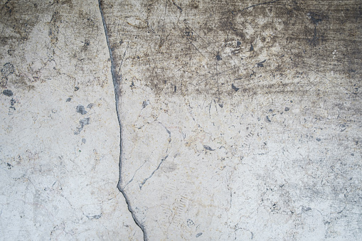 A gray weathered, dirty concrete wall with a large crack running down it.