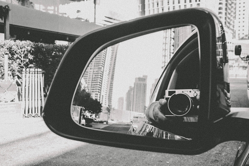 Man sticking out his vintage camera and taking photograph through rear view car mirror