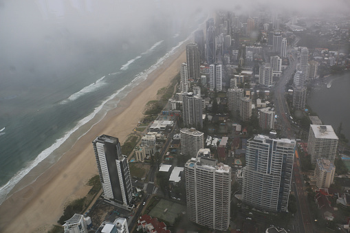 Looking through Q1 window at overcast Gold Coast cityscape alongside beach. Raindrops on glass. Looking south showing almost empty Gold Coast highway due to storm, and high-rise developments under fog and cloud.
