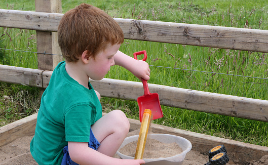 Red headed Child playing with toys in a Sand Pit